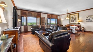 Un amplio salón con sofás de cuero, una mesa de comedor de madera y ventanas grandes con contraventanas.