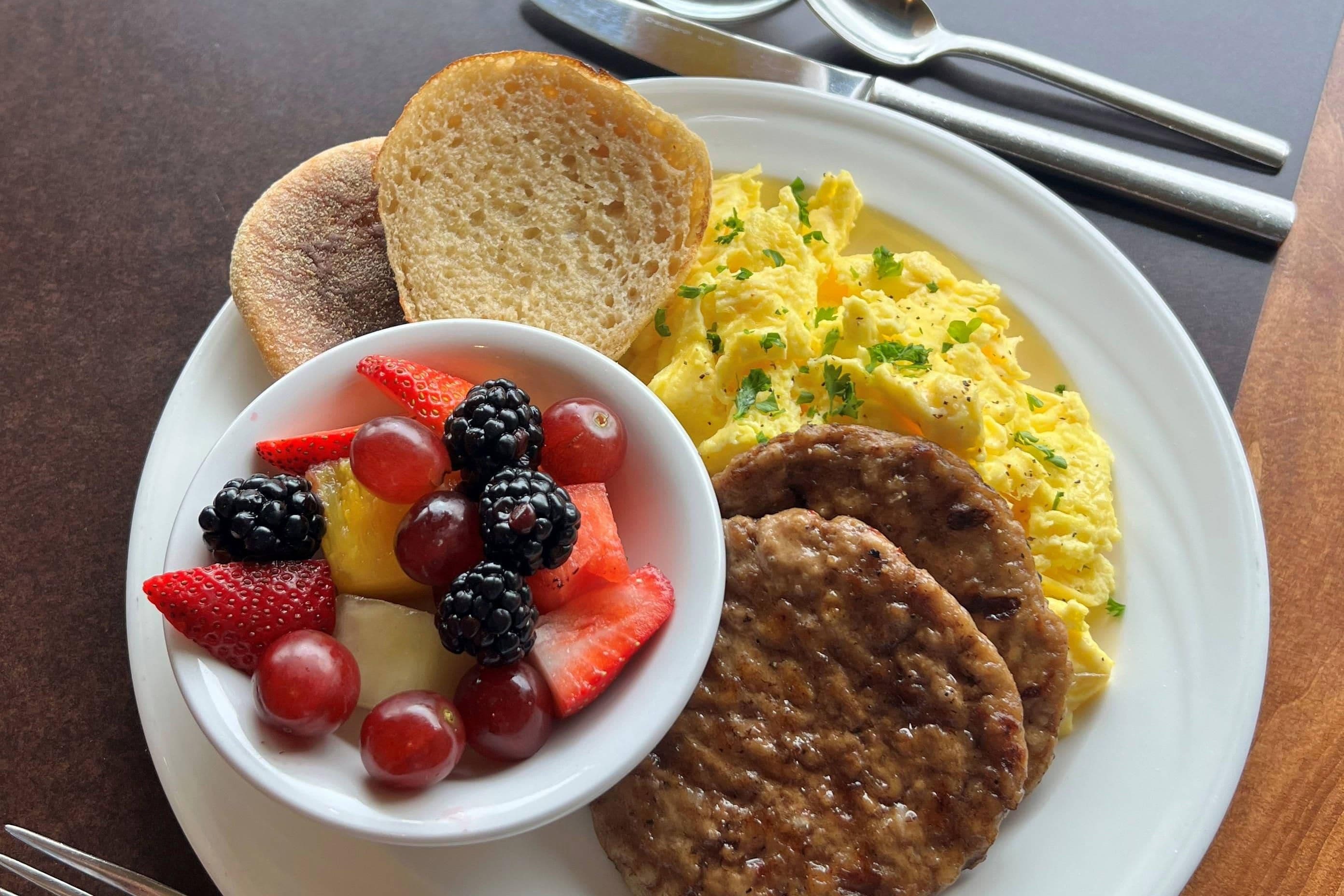 A breakfast plate with scrambled eggs, toast, fruit, and sausage patties.
