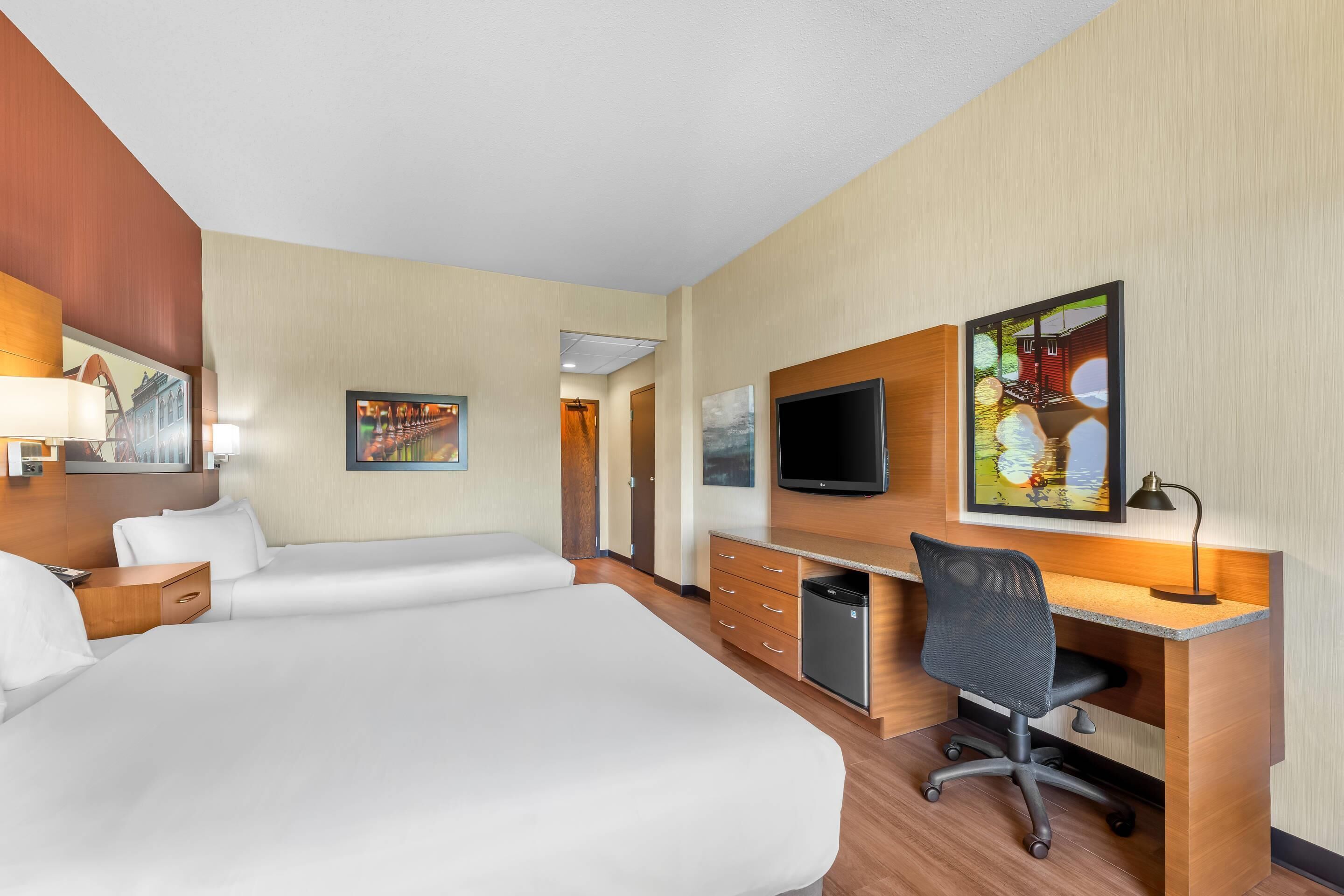 A hotel room with a large bed, a desk with a chair, a television, and artwork on the walls.