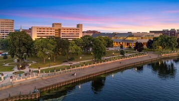 Vista al río de un hotel con un edificio moderno, un parque con árboles y un camino peatonal.