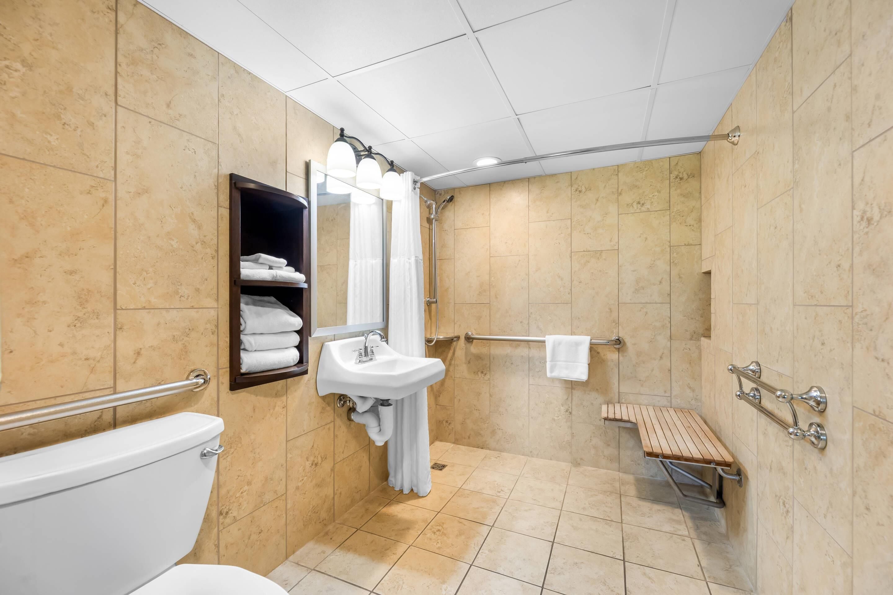Baño con inodoro, lavabo, ducha y un banco.