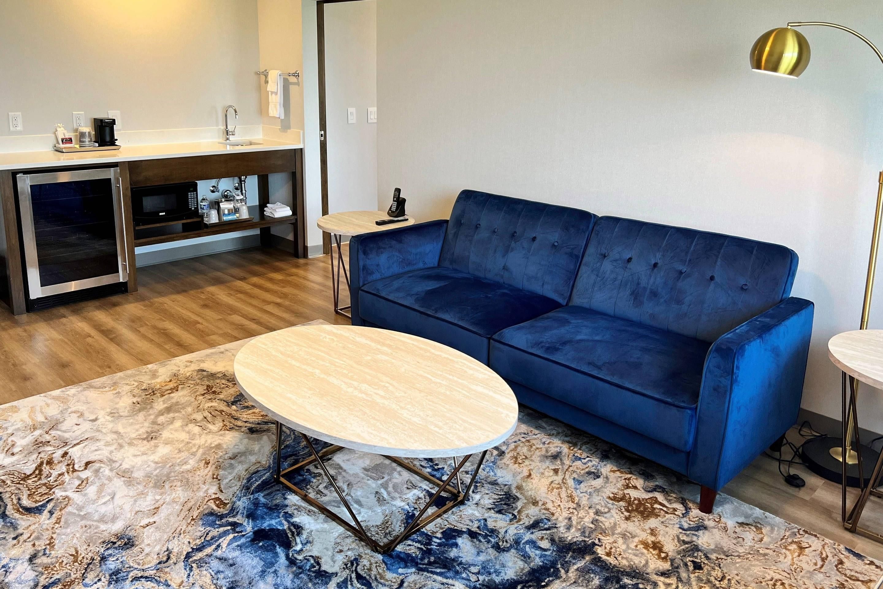 A modern living room with a blue sofa, a round coffee table, a small side table, a built-in microwave, and a pendant light.