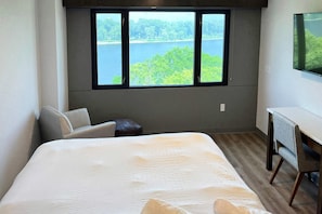 Une chambre d’hôtel avec un grand lit, un bureau, une chaise et une fenêtre donnant sur un lac et des arbres.