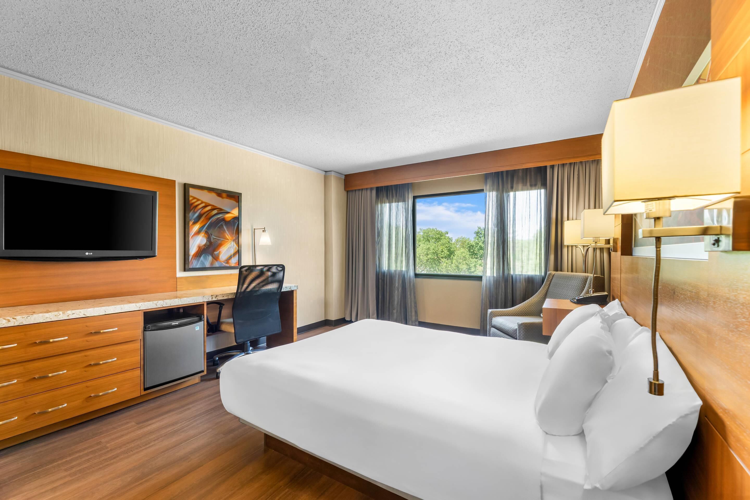 A hotel room with a bed, desk, television, and a window with curtains.