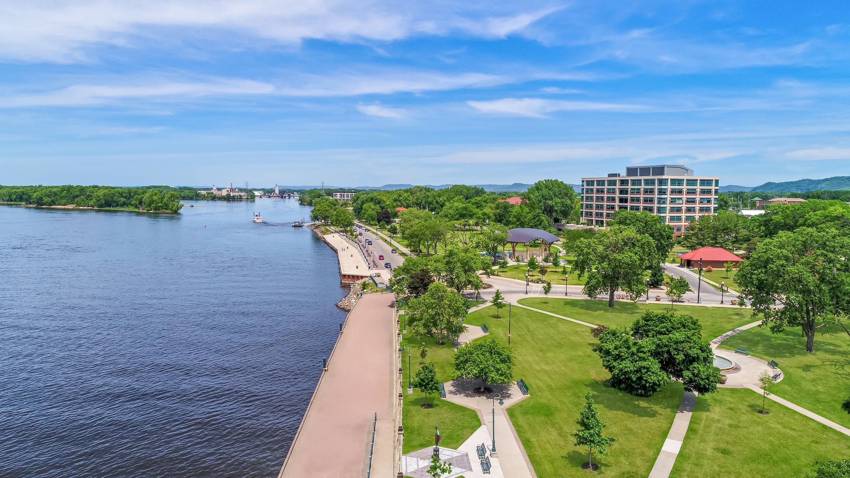 A riverside view with a park, a bridge, and a modern building.