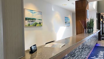A reception desk with a telephone, framed landscape pictures, and a welcome mat.