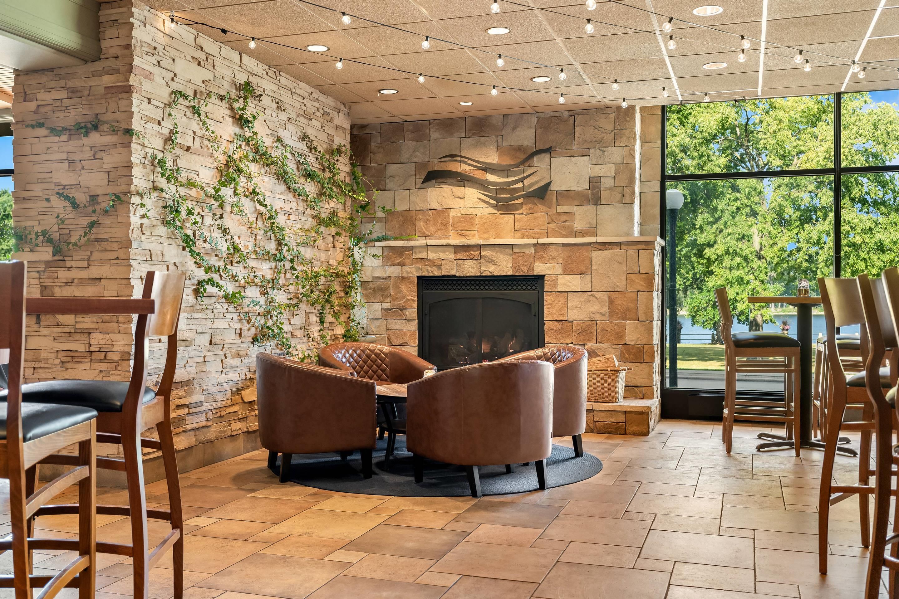 A cozy seating area with a stone fireplace, surrounded by wooden chairs and a round table.