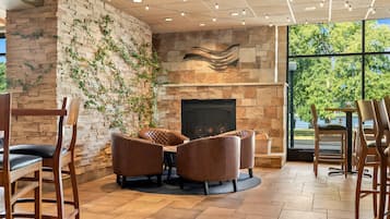 A cozy seating area with a stone fireplace, surrounded by wooden chairs and a round table.