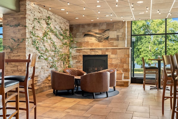 A cozy seating area with a stone fireplace, surrounded by wooden chairs and a round table. - Radisson Hotel La Crosse (La Crosse)
