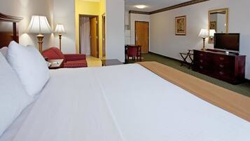 A hotel room with a large bed, a desk with a chair, a television, and a dresser.