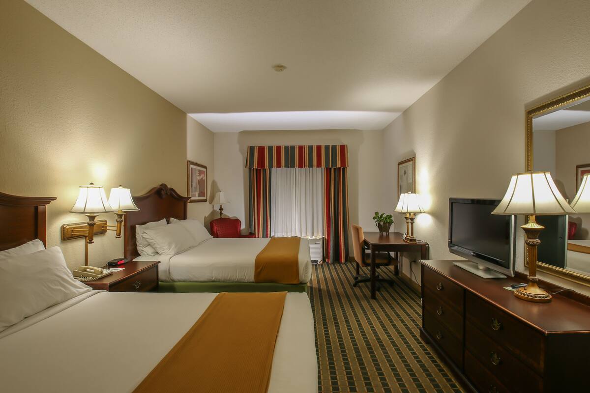 Una habitación de hotel con dos camas, televisión, escritorio, silla y cómoda.