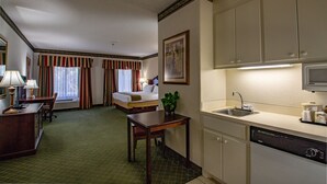 Ein Hotelzimmer mit Bett, Schreibtisch, Stuhl, einem kleinen Tisch, einer Pflanze, einem Waschbecken und einer Mikrowelle.