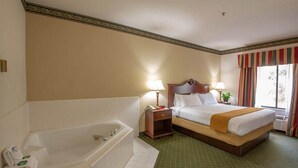 Ein Hotelzimmer mit einem großen Bett, einem separaten Badezimmer mit einer Badewanne und einem Fenster mit Vorhängen.