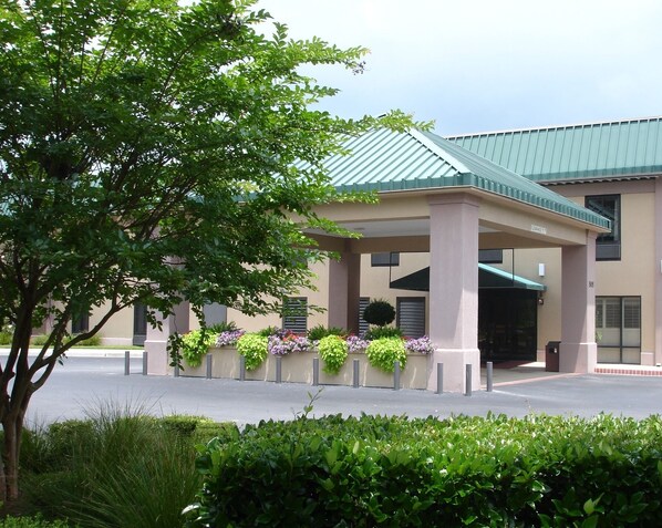 A building with a covered entrance, a green roof, and a flower bed with various plants.