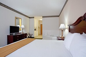 A hotel room with a large bed, a television, a desk with a lamp, a mirror, and a view into the bathroom.