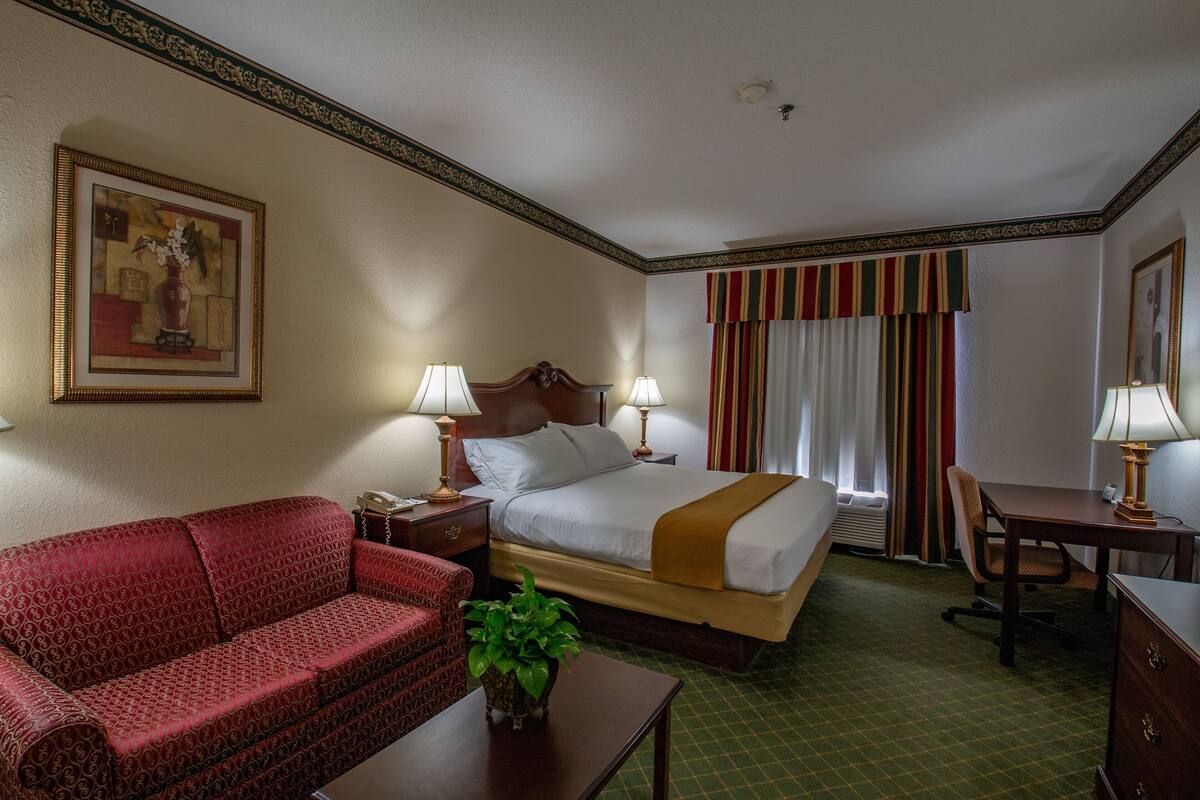 Una habitación de hotel con una cama, un sofá rojo, un escritorio y una lámpara.