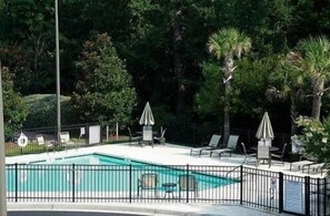 A swimming pool with a fenced area, lounge chairs, and umbrellas.