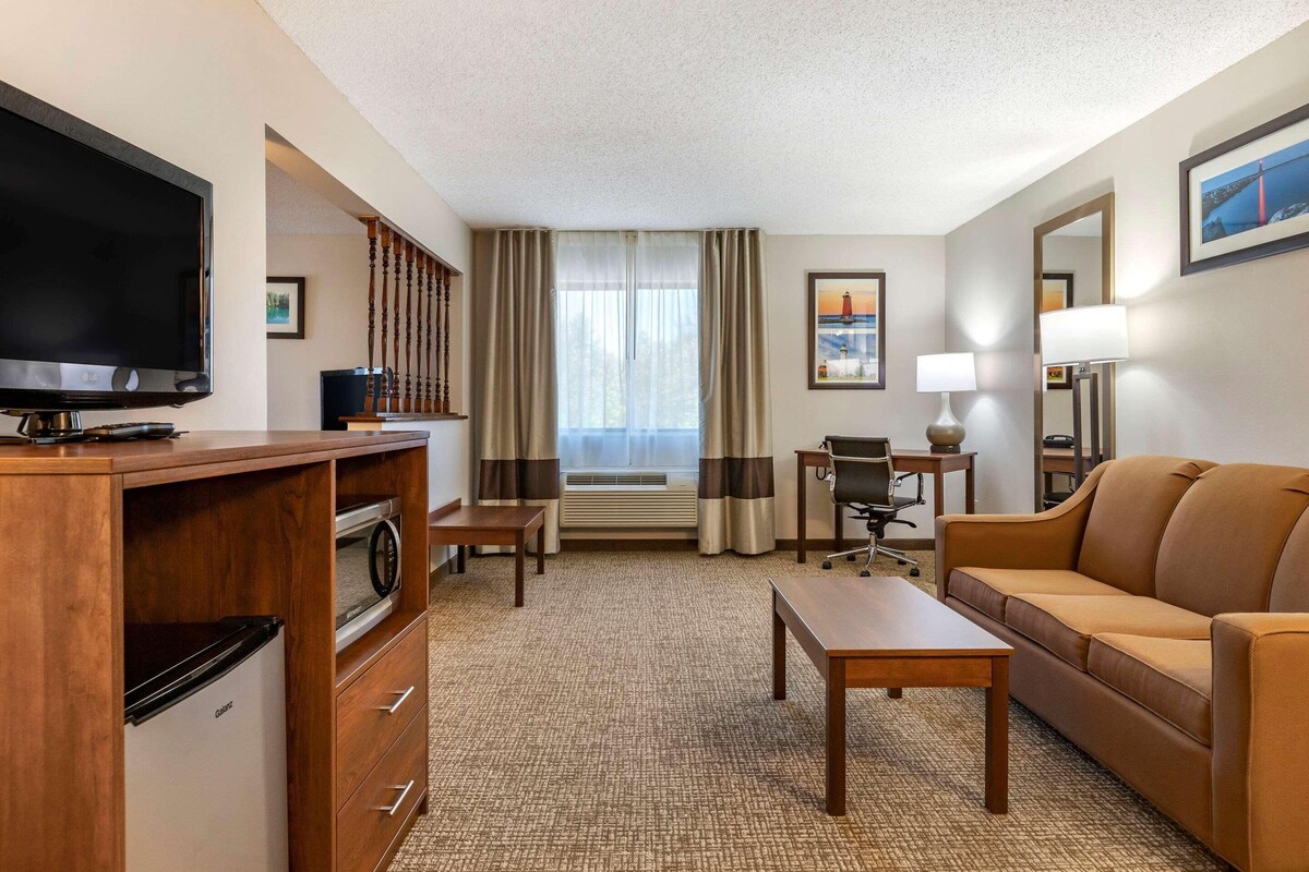 A hotel room with a television, kitchenette, seating area, and large windows.