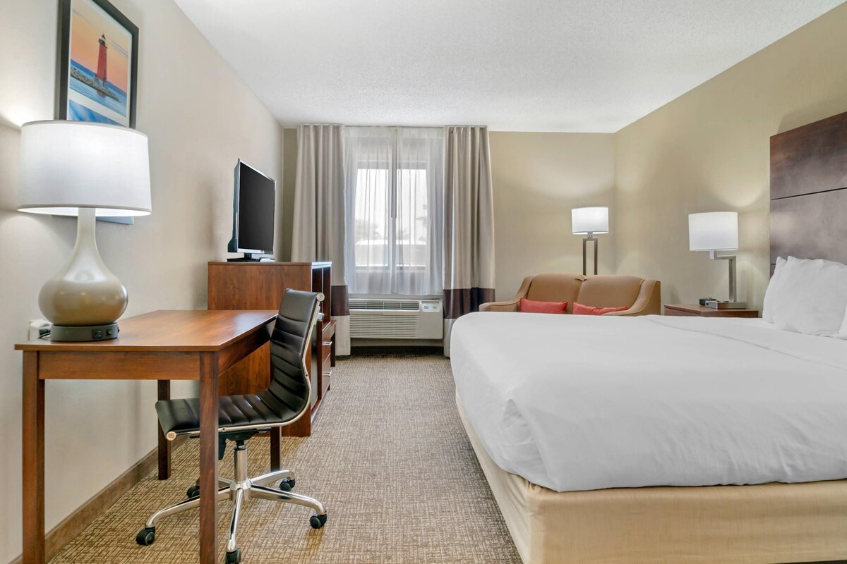 A hotel room with a bed, desk, chair, television, and a window with curtains.