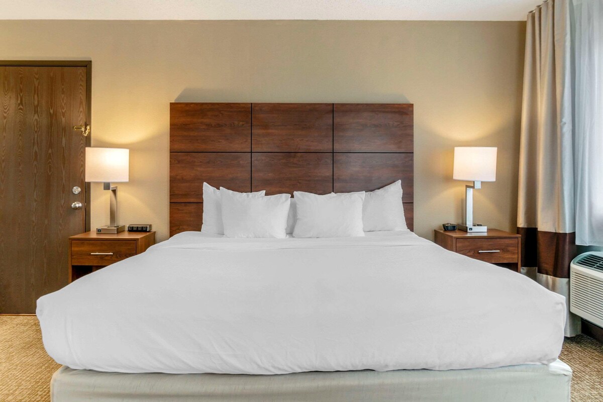 A neatly made bed with white linens, two bedside tables with lamps, a wooden headboard, and a door to the left.