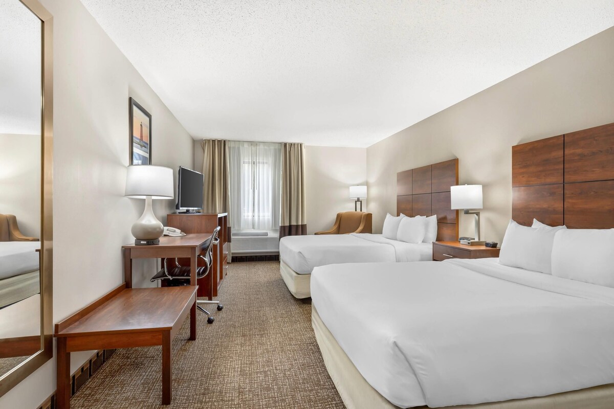 A hotel room with two beds, a desk, a chair, a TV, and a window with curtains.