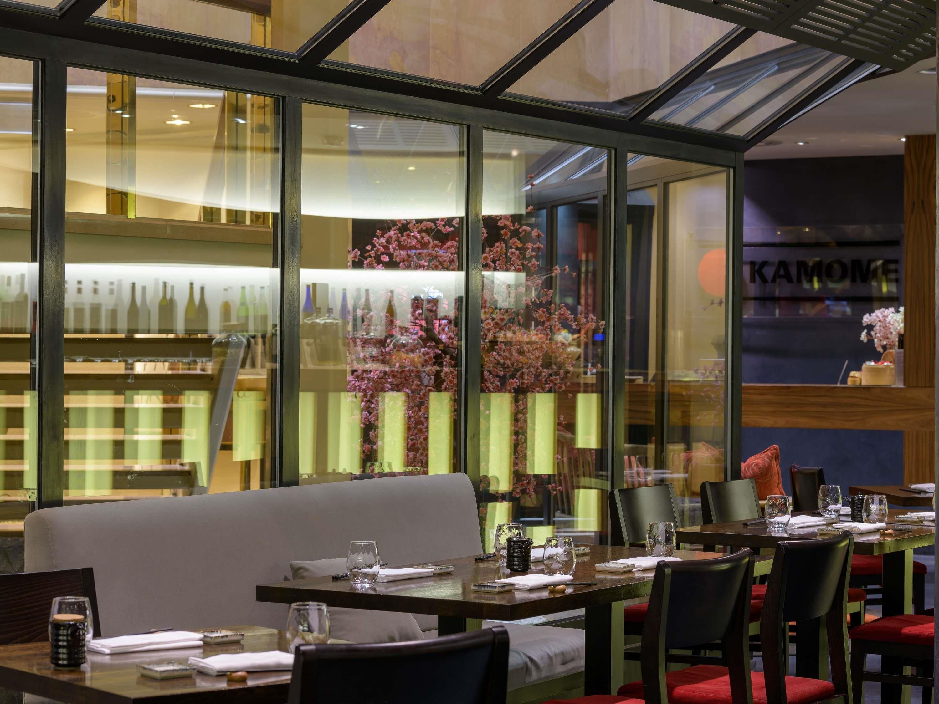 Un restaurant doté d’un mur en verre, de tables dressées avec des verres à vin, et dont la décoration inclut des bouteilles visibles en arrière-plan.