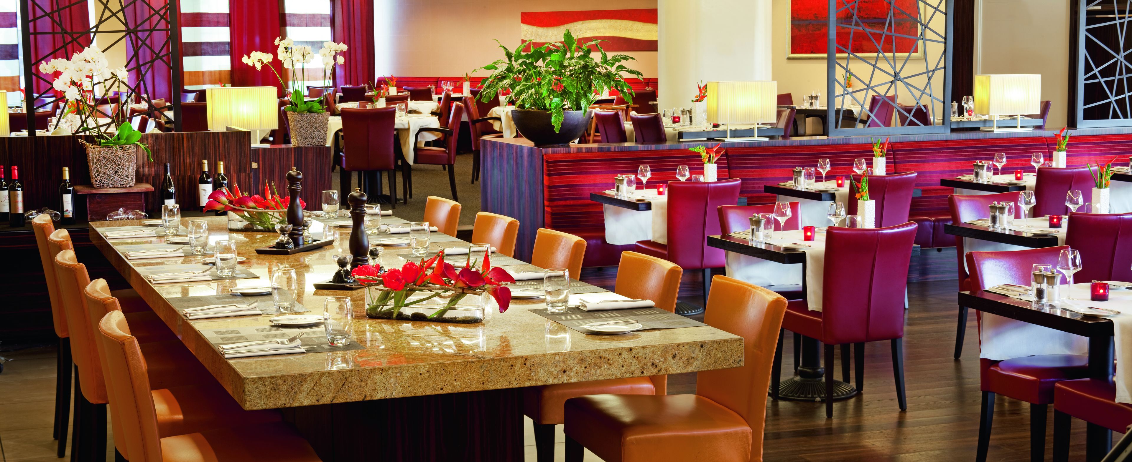 Un restaurant avec de nombreuses tables et chaises, un long comptoir et des plantes en pot.