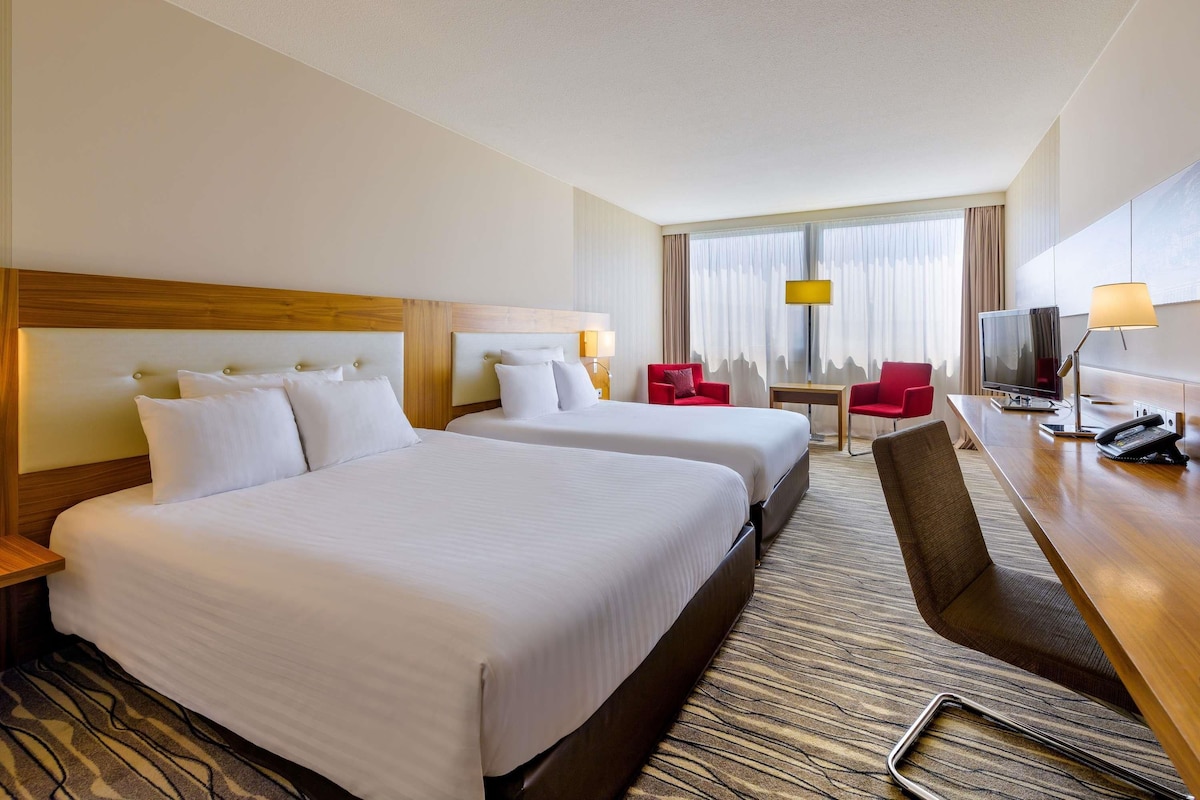 Habitación de hotel con dos camas, un escritorio con televisor, una silla y una lámpara.