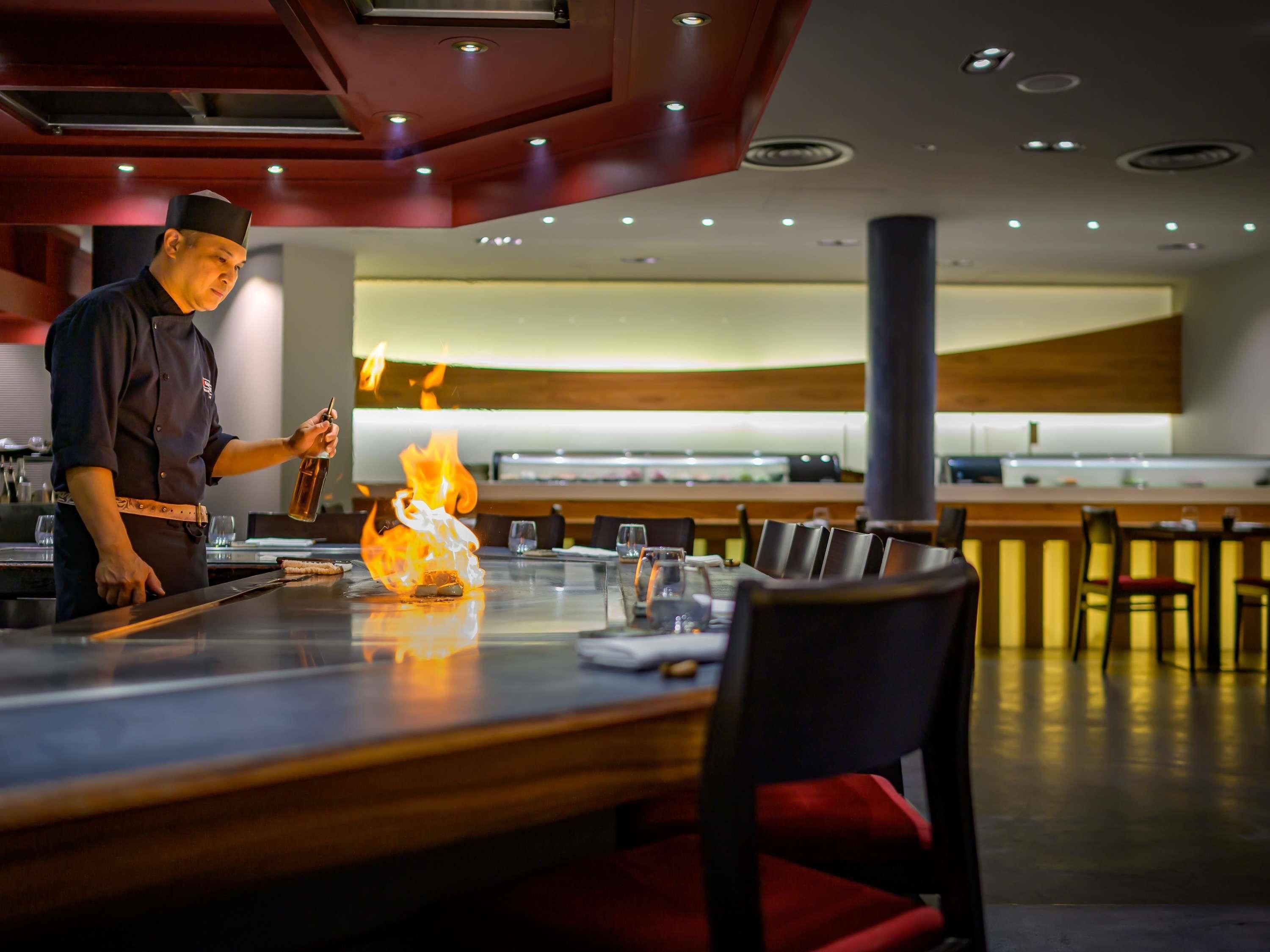 A modern restaurant interior with a bar area, seating arrangement, and a chef performing a flambé.