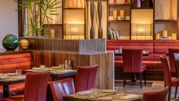 A restaurant with red leather chairs, wooden tables, and a variety of decorative vases and plants.