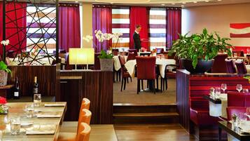 Un restaurant doté de nombreuses tables, de chaises à revêtement rouge et de plantes en pot.