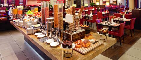 Un espace buffet proposant divers plats et un coin salon avec des chaises et des tables rouges.
