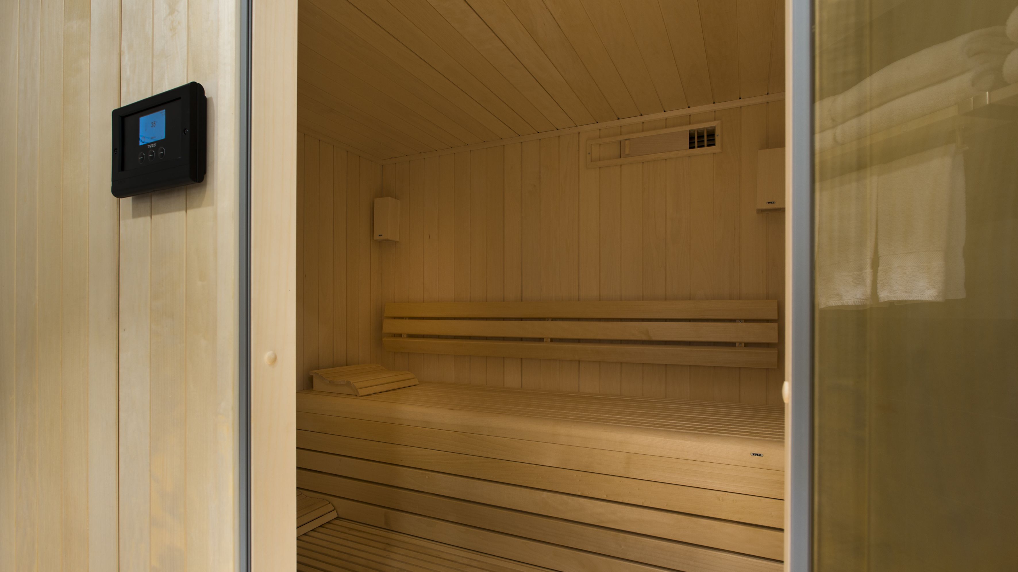 A sauna with wooden benches and a control panel on the wall.