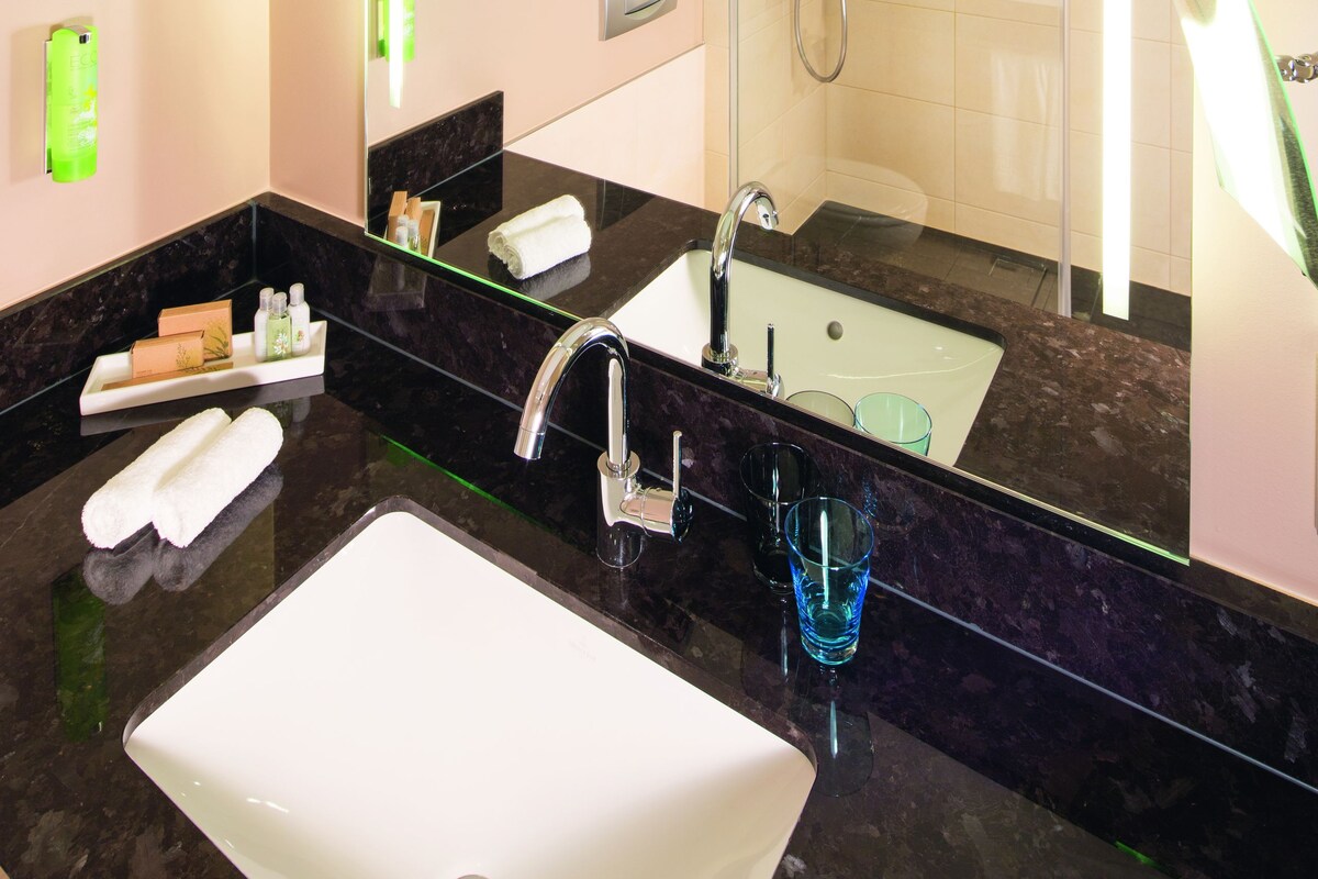 A modern bathroom with a large mirror, a sink, a shower, and a glass door.