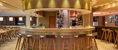 Zona de bar moderna con diseño circular, taburetes y un área de estar con mesas y sillas.