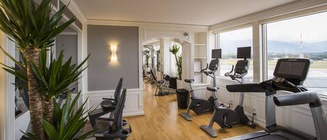 A home gym with various exercise equipment, a large window with a view of the outdoors, and a potted plant.