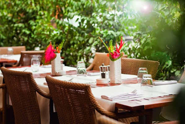 A restaurant with wicker chairs and tables set for dining, surrounded by greenery. - Mövenpick Hotel Geneva (Meyrin)