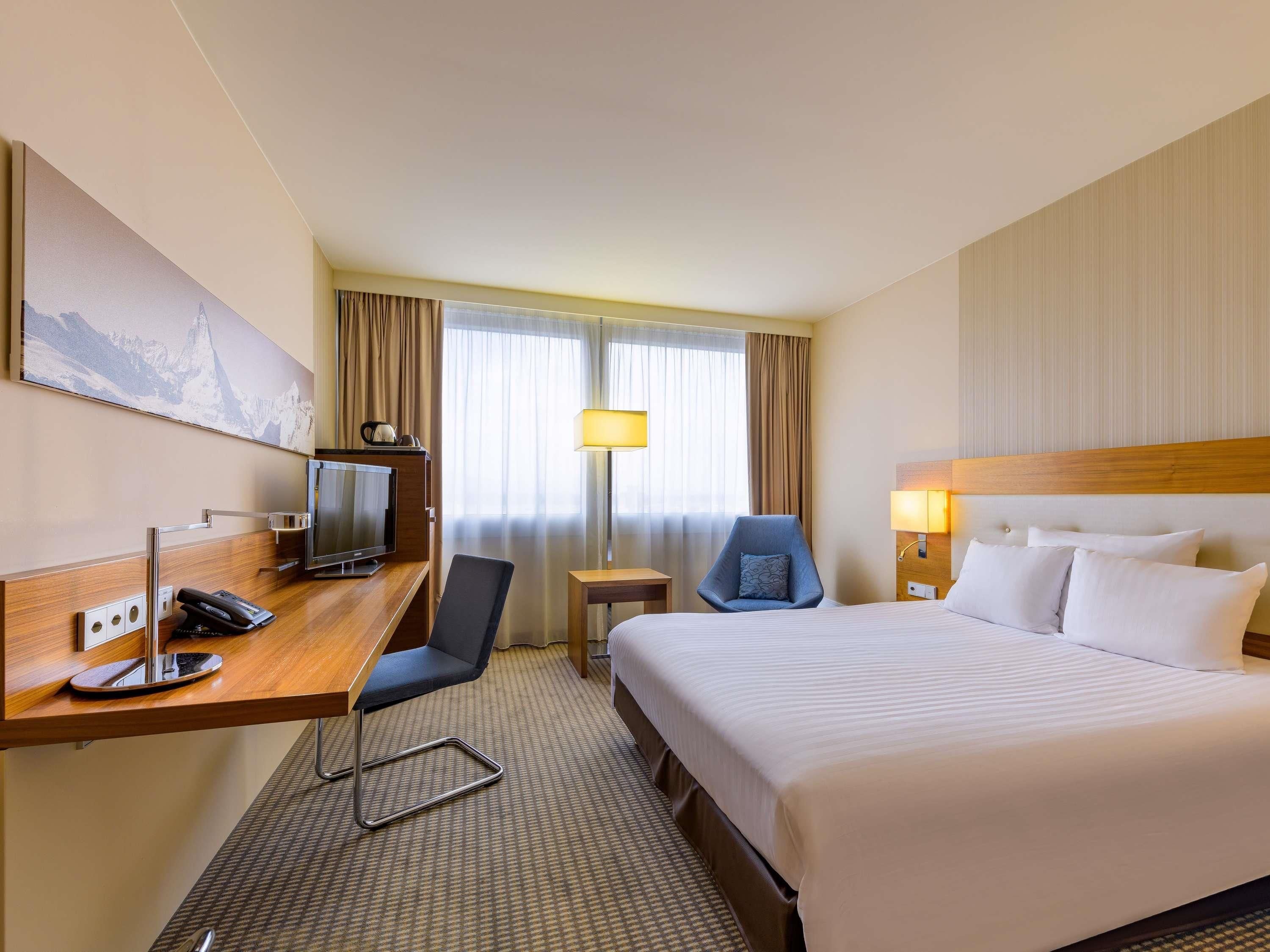 Una habitación de hotel con cama, escritorio, silla, televisión y un cuadro en la pared.