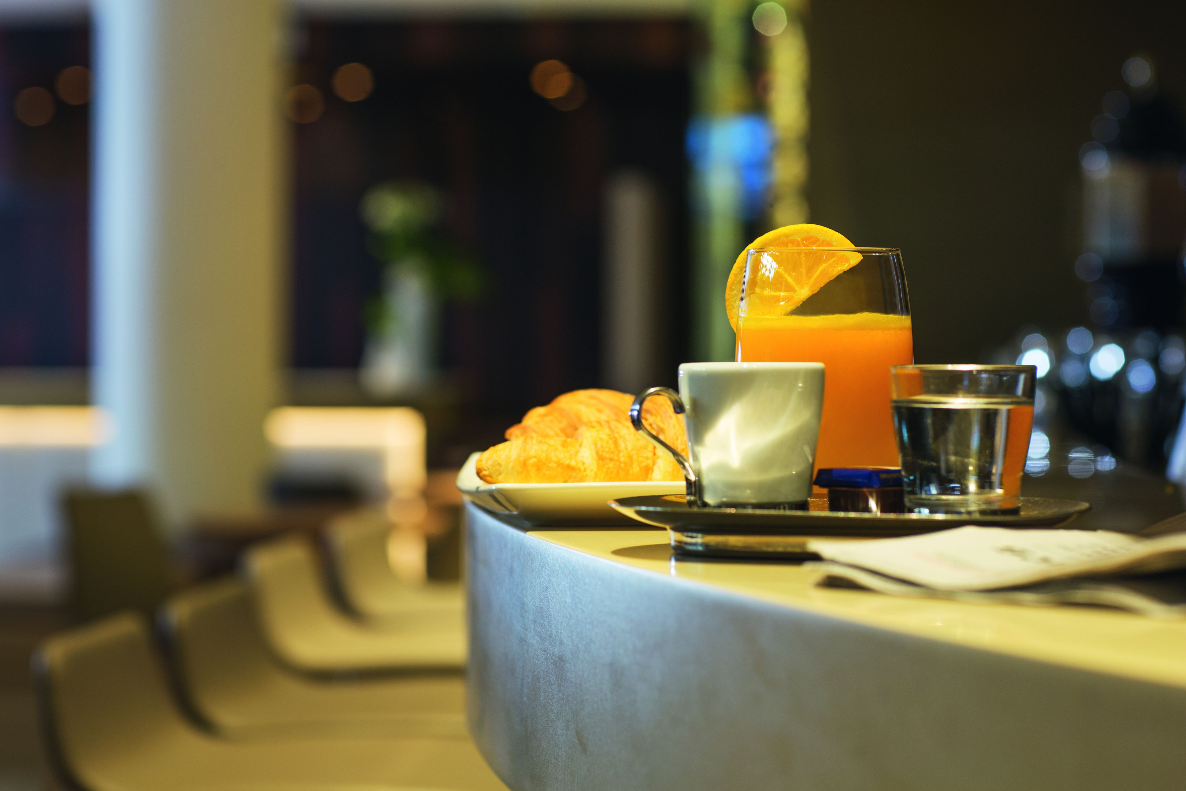 A breakfast setting with a croissant, a glass of orange juice, and a cup on a tray.