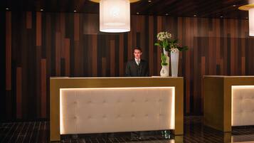 A reception area with a modern design, featuring a wooden panel wall, a large illuminated reception desk, and a vase with flowers.