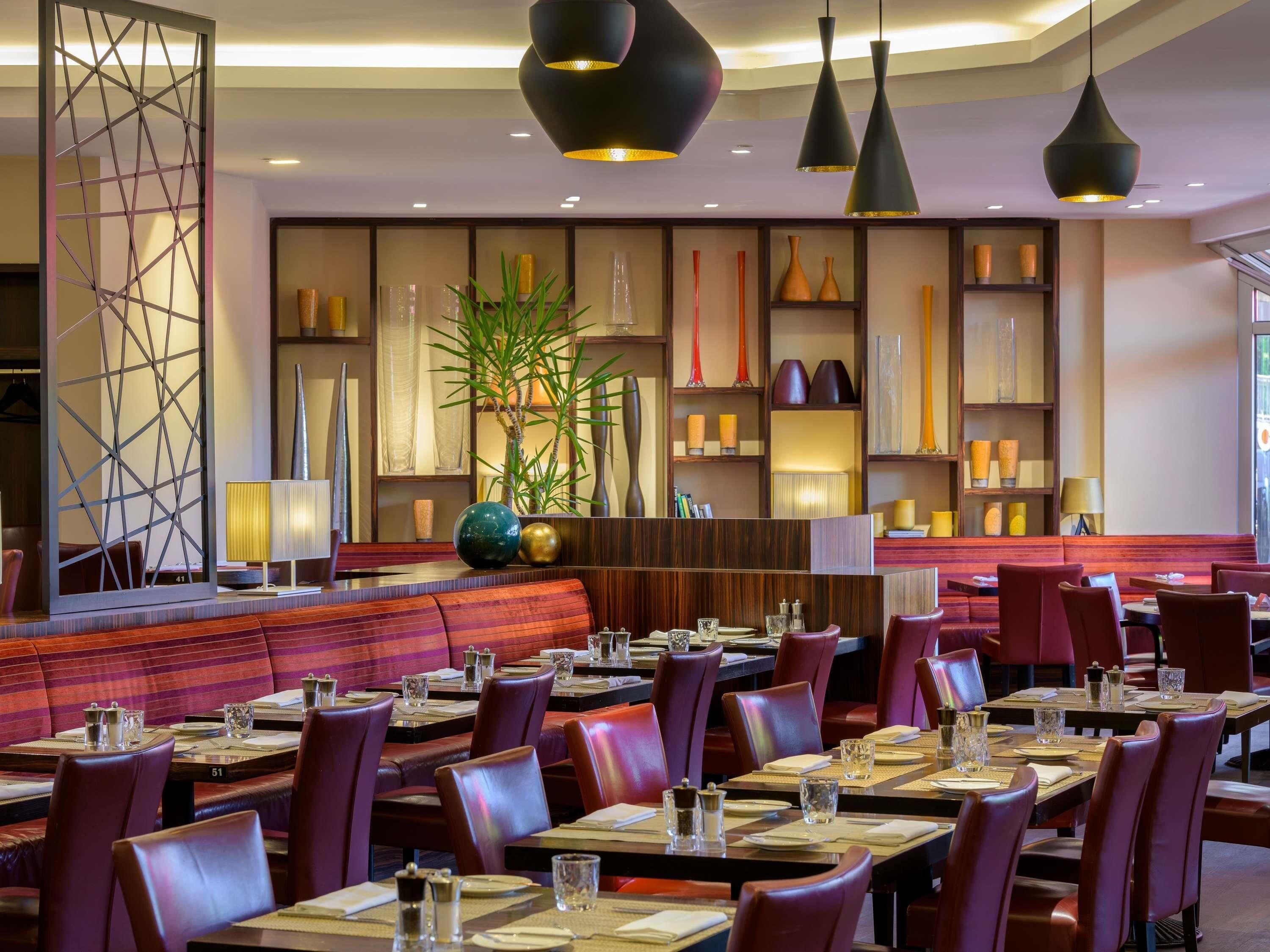 Un restaurante con mesas y cabinas, iluminación colgante y jarrones decorativos en estantes.