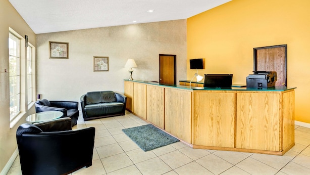 A reception area with a wooden counter, black leather chairs, a small table, and a lamp.