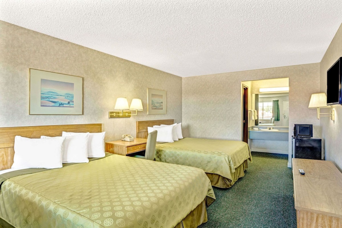 A hotel room with two beds, a desk, a TV, and a bathroom visible through an open door.