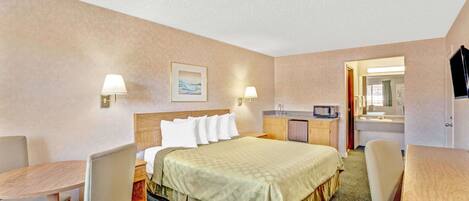 Habitación de hotel con cama, dos mesitas de noche, un escritorio, una silla, una pequeña kitchenette y un baño visible a través de una puerta abierta.