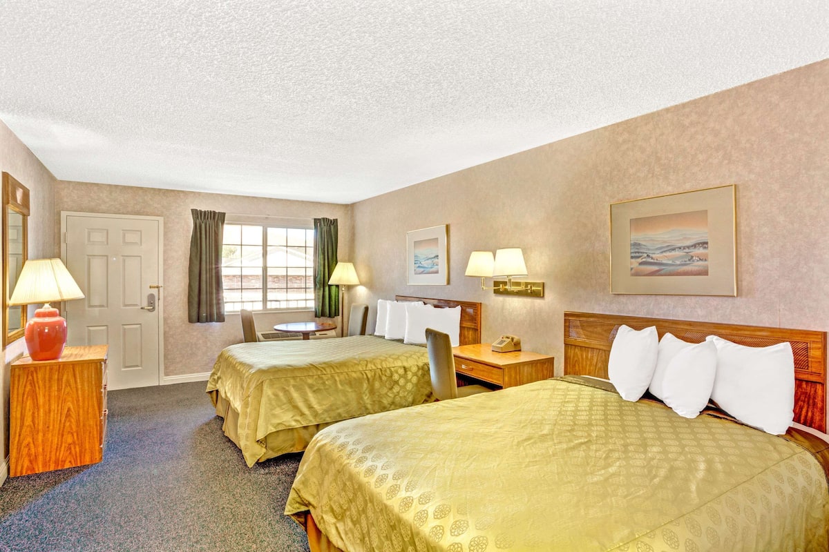 A hotel room with two beds, a desk, a chair, a lamp, and a painting on the wall.