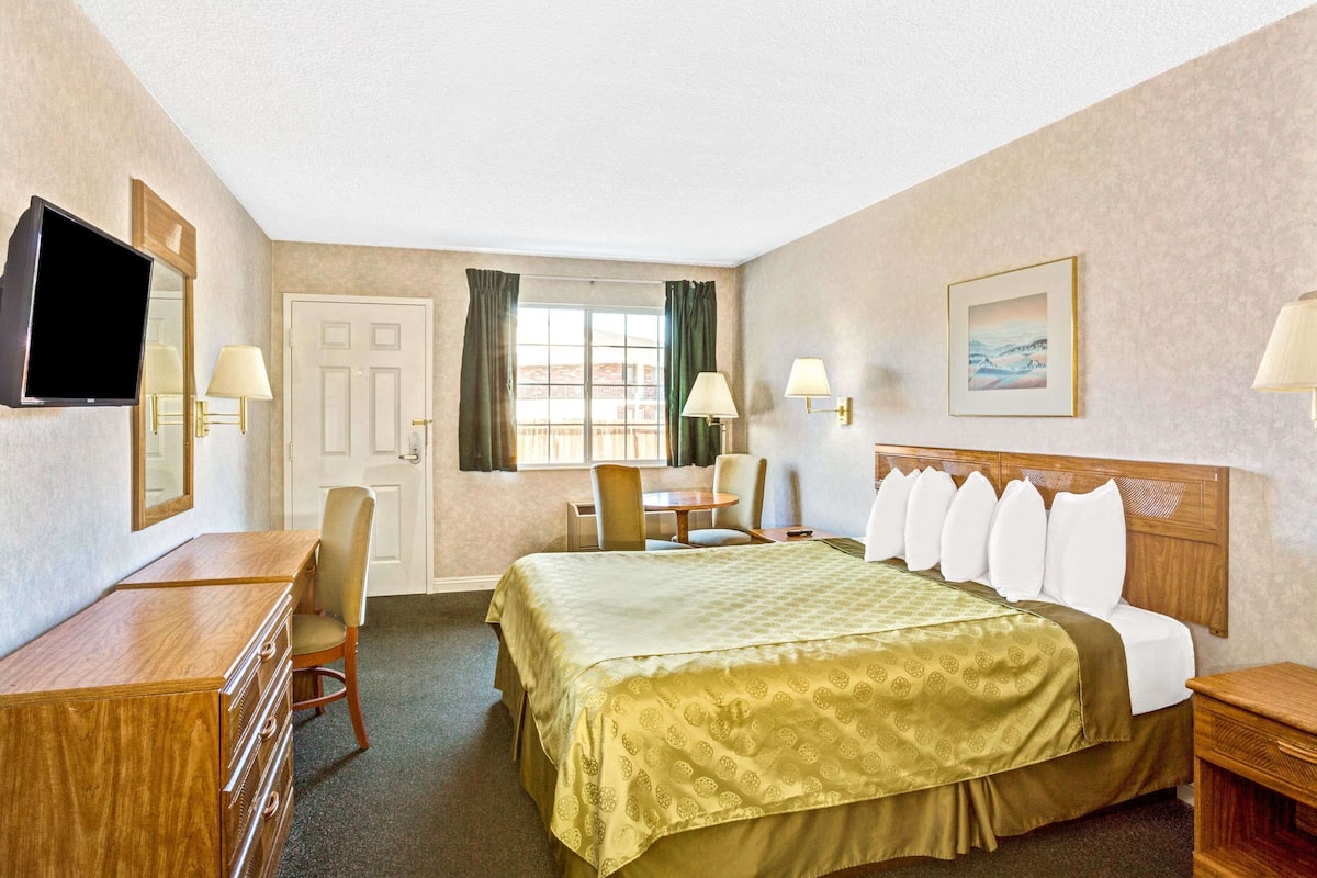 A hotel room with a bed, a desk, a chair, a television, and a window with curtains.