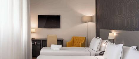 Une chambre d’hôtel avec deux lits, un téléviseur à écran plat, un bureau avec une lampe, une chaise et un mur décoré d’un motif.