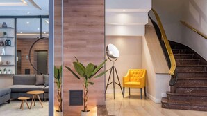 A modern living room with a sectional sofa, two wooden side tables, a potted plant, a floor lamp, a yellow armchair, and a staircase with a golden handrail. - Hotel Madrid Plaza de España Affiliated by Meliá (Madrid)