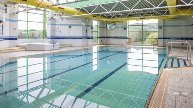 An indoor swimming pool with clear water, tiled walls, and a view of greenery outside. - Holiday Inn Stoke on Trent M6, Jct 15 by IHG (Newcastle-Under-Lyme)