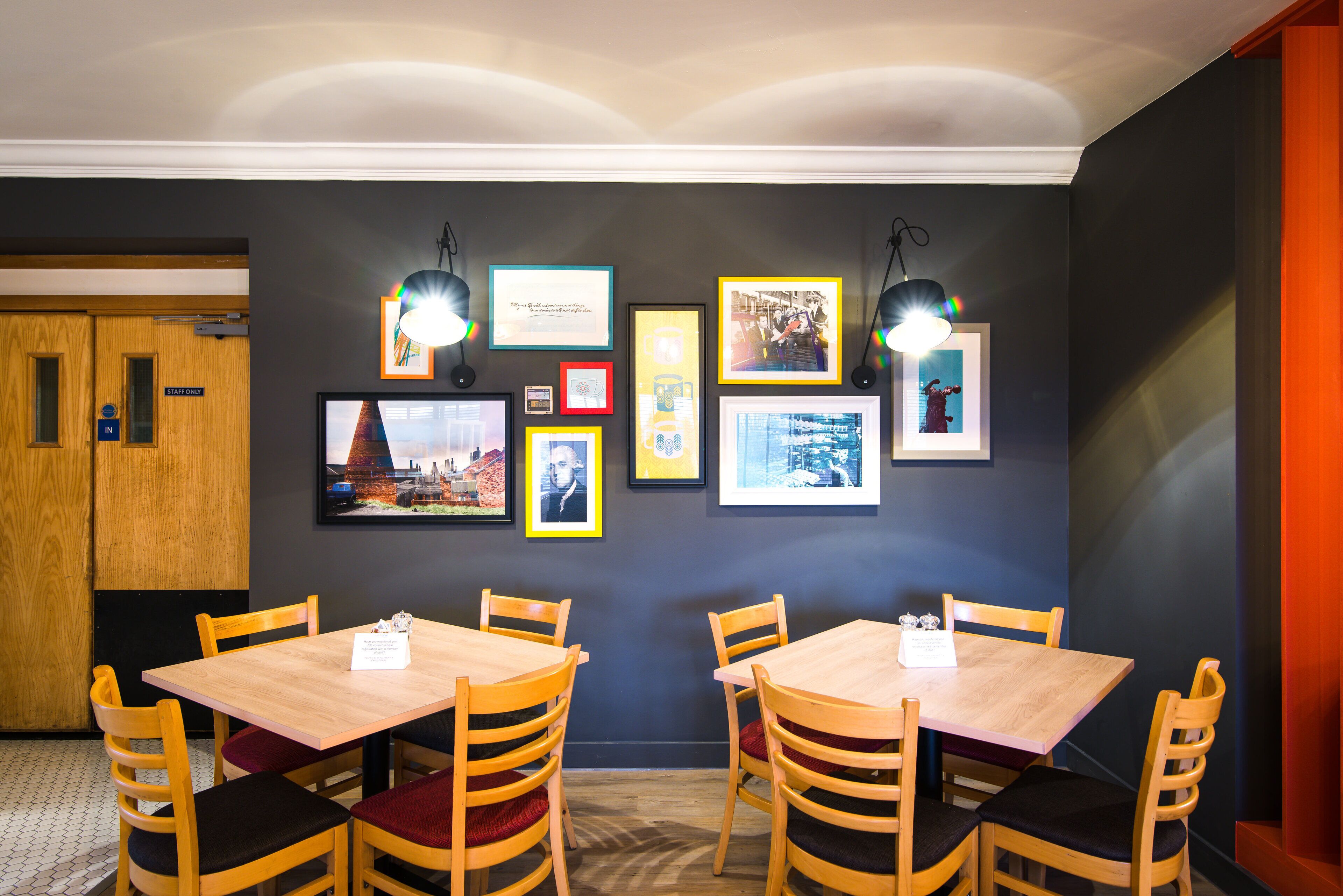 A dining area with wooden tables and chairs, framed pictures on the wall, and a sign indicating the staff room.